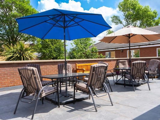 Outdoor seating area with umbrellas and tables at The Withins Residential Home.