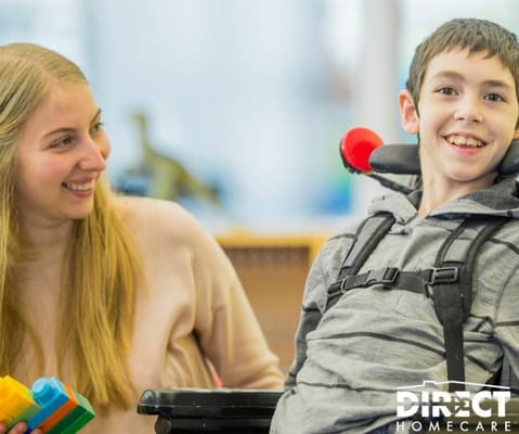 A caregiver and a child smiling and playing with building blocks