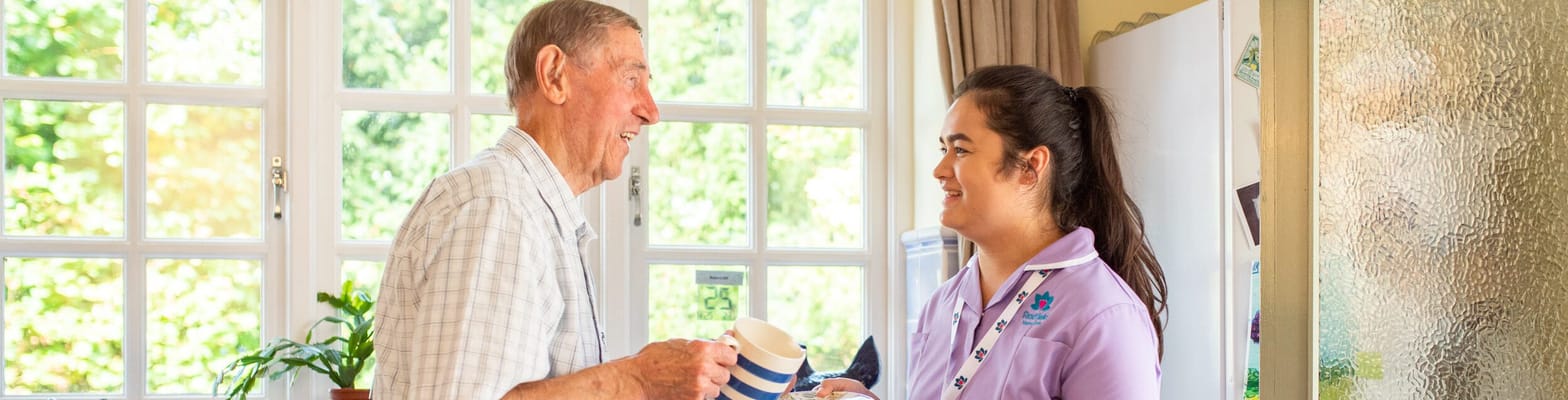 A senior man and a caregiver share a warm moment over cups of tea.