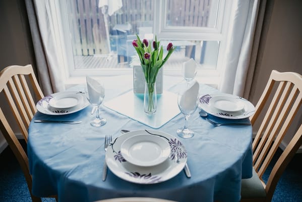 Dining table set with dishes and flowers by a window