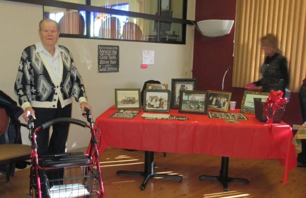 Elderly man with a walker standing next to a table displaying framed photos at Evergreen.