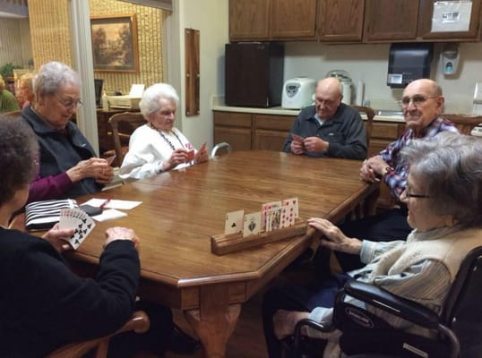 Seniors playing cards around a table in a communal room