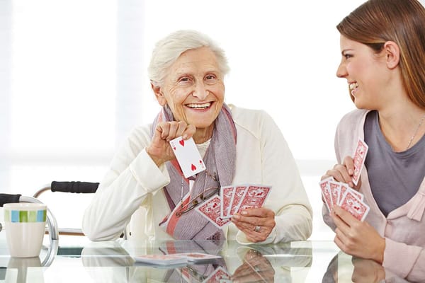 Senior woman playing cards with a staff member