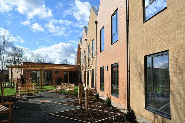 Exterior view of Brook Meadows House with landscaped garden and benches