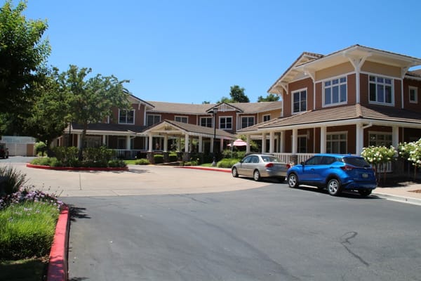 Front entrance of Sunrise of Carmichael with cars parked and greenery