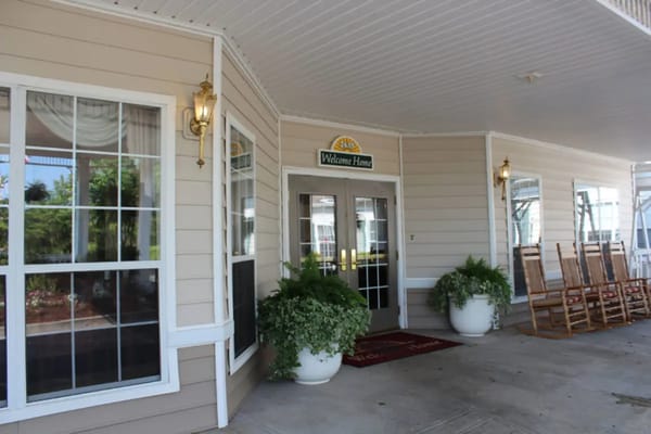 Front entrance of Lakes at Gainesville Assisted Living featuring a welcome sign and rocking chairs.