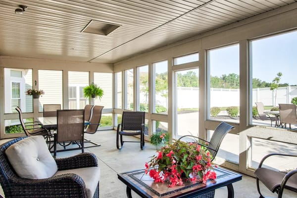 A bright screened porch with seating and potted plants.