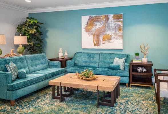 A cozy living room featuring teal sofas, a wooden coffee table, and decorative plants.