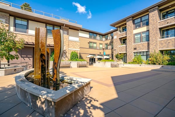 A tranquil courtyard featuring a modern water fountain surrounded by lush greenery.