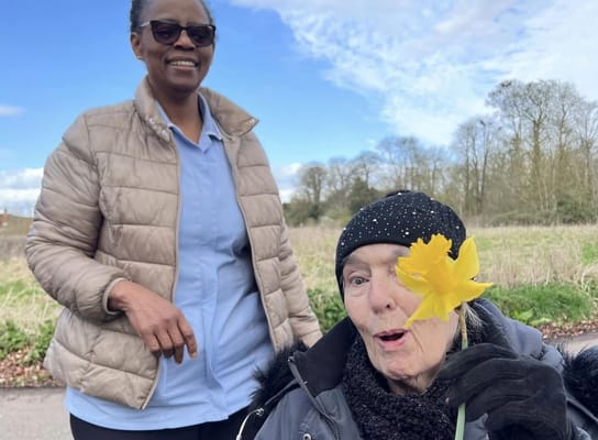 Resident enjoying a flower outdoors with staff member