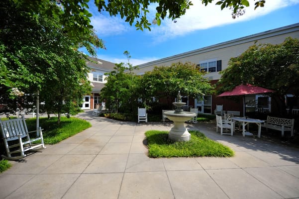 A serene courtyard featuring a fountain, green landscaping, and seating areas.