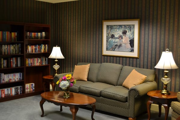 A cozy living room with a couch, coffee table, lamp, and bookshelf filled with books.