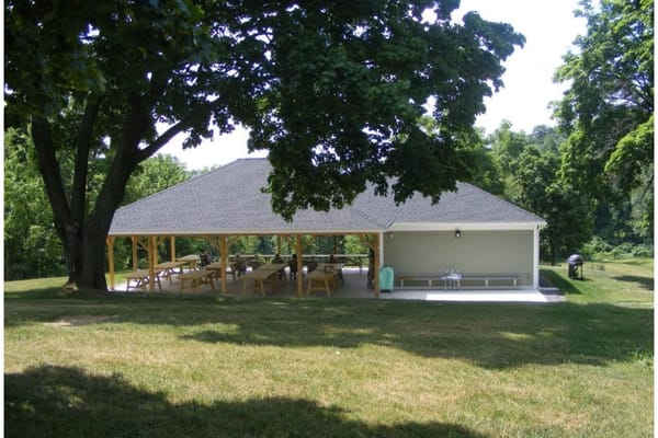 Outdoor pavilion with picnic tables under large trees