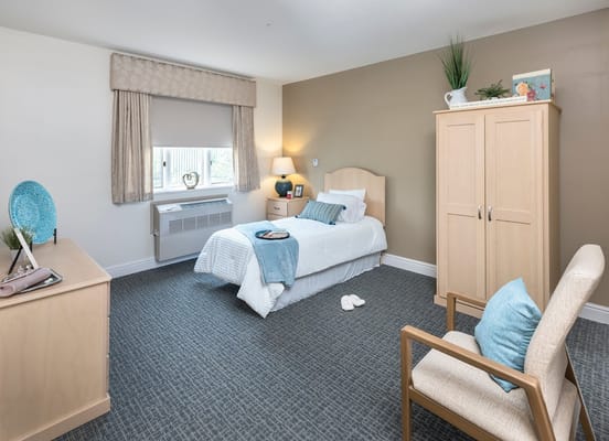 A bright, cozy bedroom with a bed, chair, and dresser in Overlook Green Senior Living.