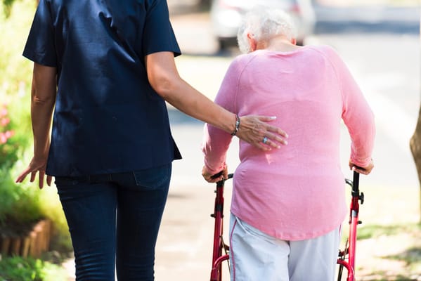 Caregiver assisting a resident with a walker outside