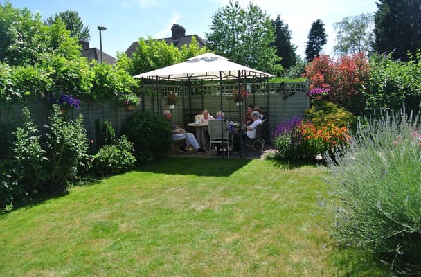 Group of seniors sitting at a table under a gazebo in a garden.