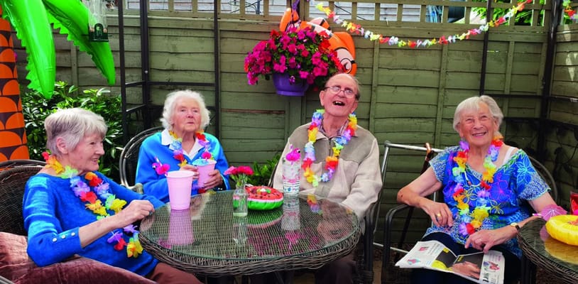 Four residents at St. Andrew's enjoying a festive gathering with leis and drinks.