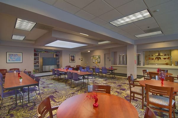 A spacious dining and activity area with tables and chairs, vibrant decor, and a TV.