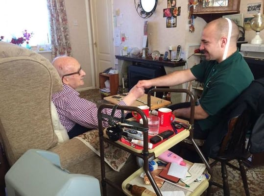 An elderly man and a caregiver shaking hands in a cozy living room