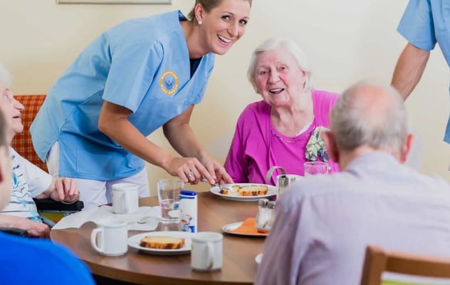 Staff serving food to smiling residents in a dining area
