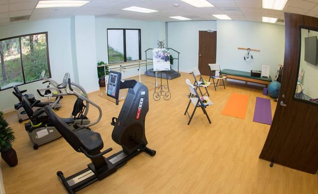 A spacious fitness room with exercise equipment and mats.
