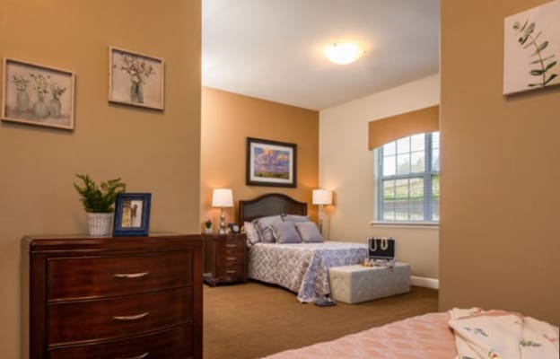 Cozy bedroom in Silverado Overland Park Memory Care Community with a bed and wooden dresser.