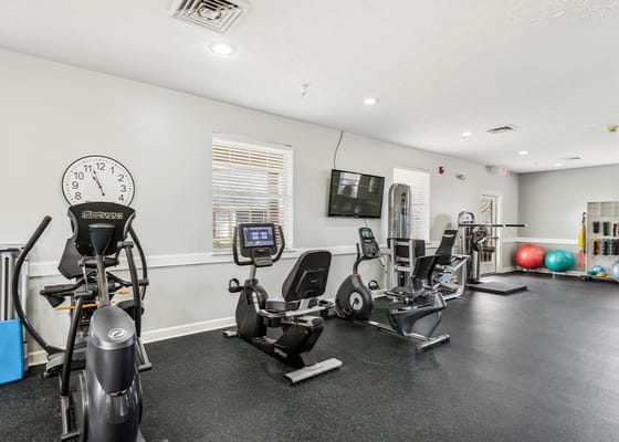 Bright fitness center with exercise equipment and large clock.