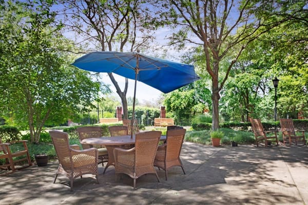 Outdoor patio with a blue umbrella and wicker furniture surrounded by greenery.