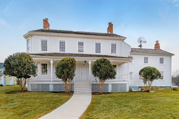 Front view of a historic white house with a porch and manicured shrubs