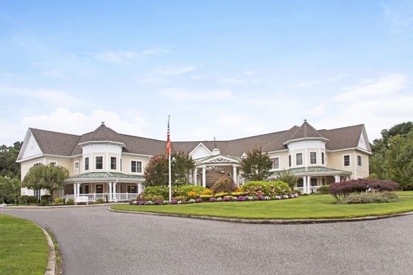 Front view of Sunrise of Dix Hills senior living facility with gardens