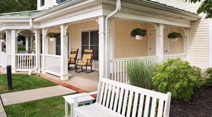 Porch area with rocking chairs and hanging plants at Sunrise of Glen Cove