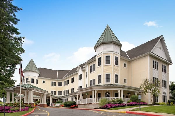 The exterior of Sunrise of Glen Cove showcasing a charming building with a peaked roof and landscaped entrance.
