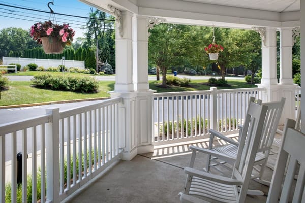 View of the porch with rocking chairs and hanging flower baskets at Sunrise of Granite Run.