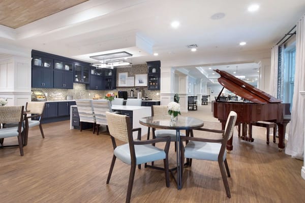 A spacious common area with a grand piano and dining tables.