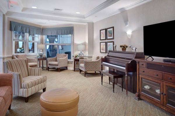 Comfortable living room with chairs, a piano, and art on the walls.