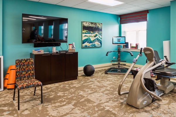 Bright fitness room equipped with exercise machines and a TV.