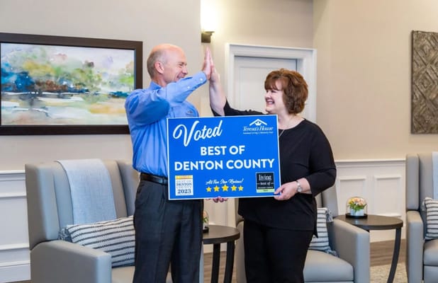 Two staff members high-fiving while holding an award sign