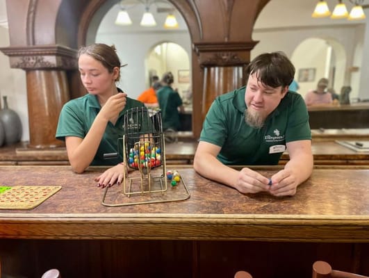 Two staff members engaged in a bingo game at a counter with colorful balls.