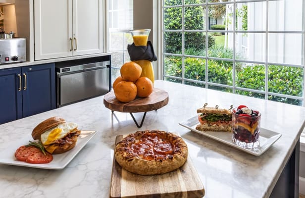 A display of breakfast and lunch items including a sandwich, pizza, and a fruit dish on a marble countertop.