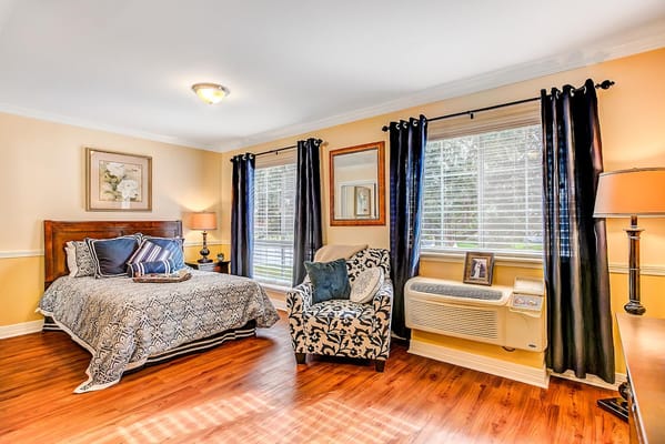 A cozy bedroom with a bed, armchair, and large windows.