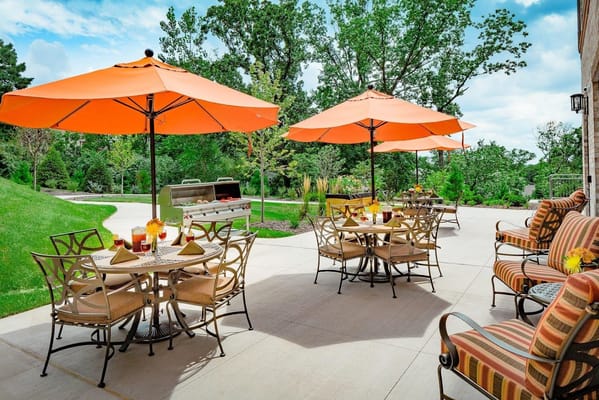A sunny outdoor dining area with orange umbrellas and tables at The Grande At Laumeier Park.