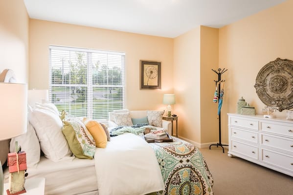 A well-furnished bedroom with a bed, decorative pillows, and a window.
