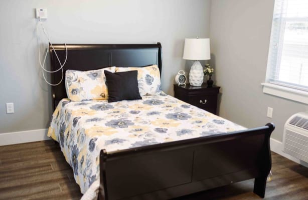 A neatly arranged bedroom with a floral comforter and bedside lamp.