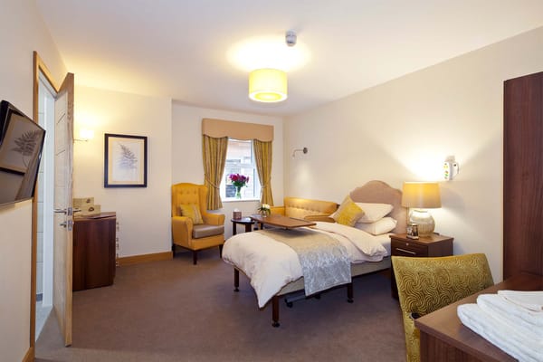 A well-furnished private room with a bed, armchair, and natural light.