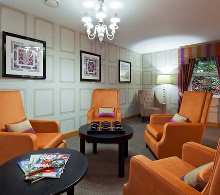 Lounge featuring orange armchairs, a coffee table with magazines, and decorative artwork on the walls.