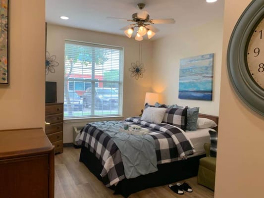 A cozy bedroom featuring a bed with a checkered duvet, a dresser, and a window with blinds.