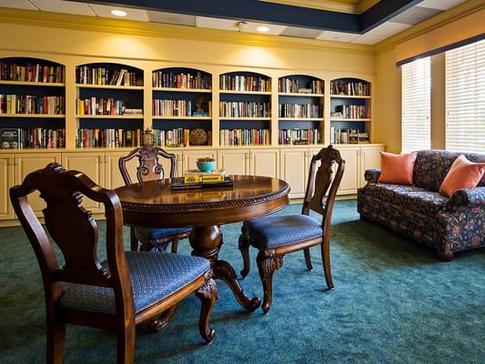 Elegant reading room featuring a round table, chairs, and bookshelves filled with books.