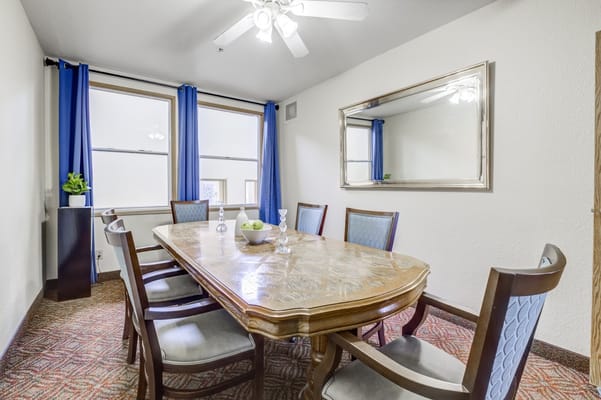 A spacious dining room with a wooden table and chairs, large windows, and blue curtains.