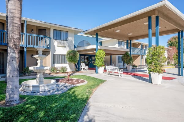 Main entrance of a senior living facility with lush greenery and a fountain