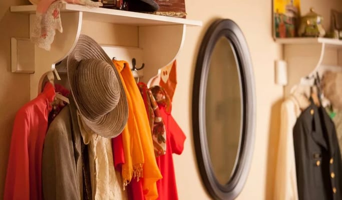 A hallway shelf displaying a variety of colorful clothing and a large mirror.